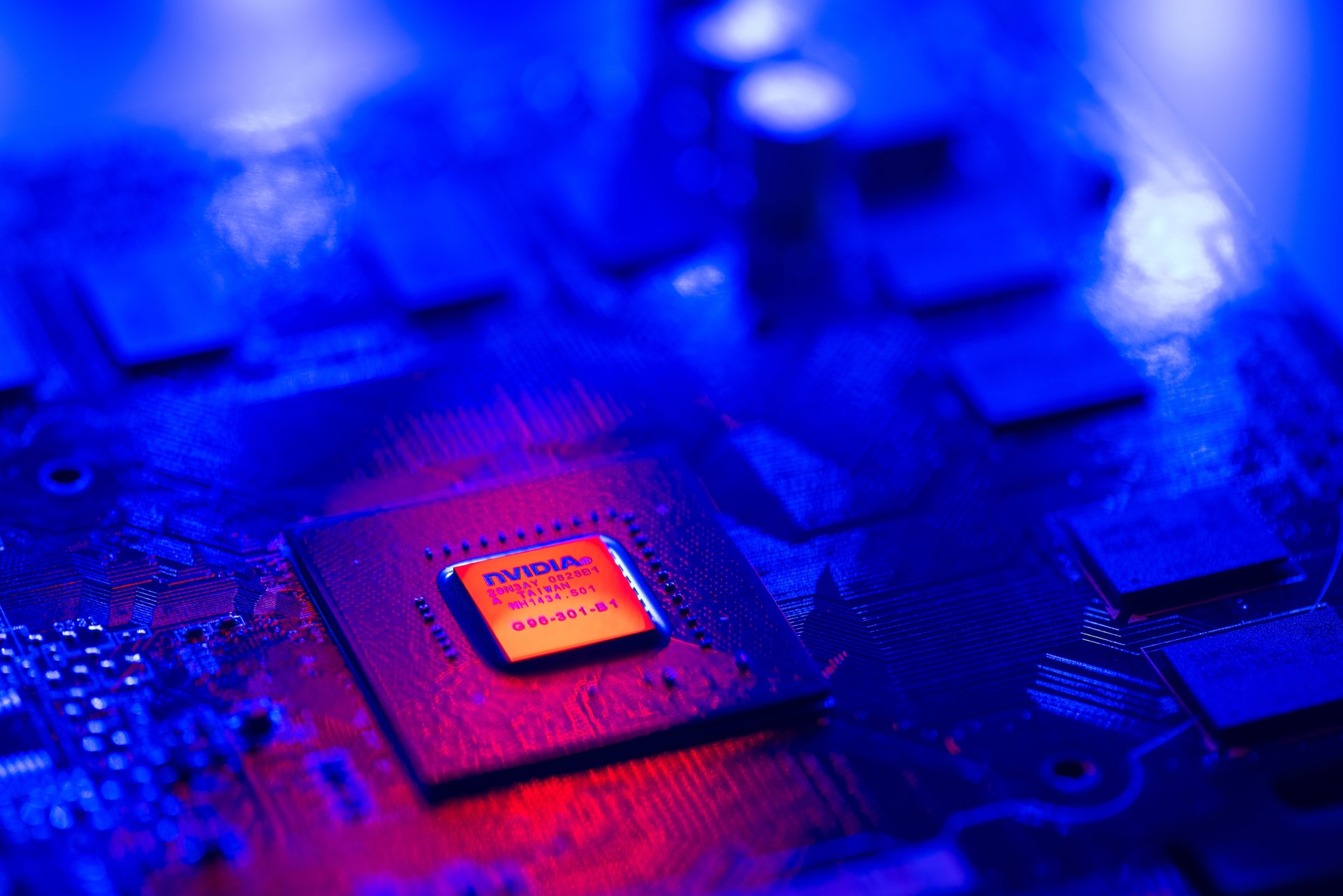 Computer chip board in blue light with an NVIDIA chip in the middle lit up orange.