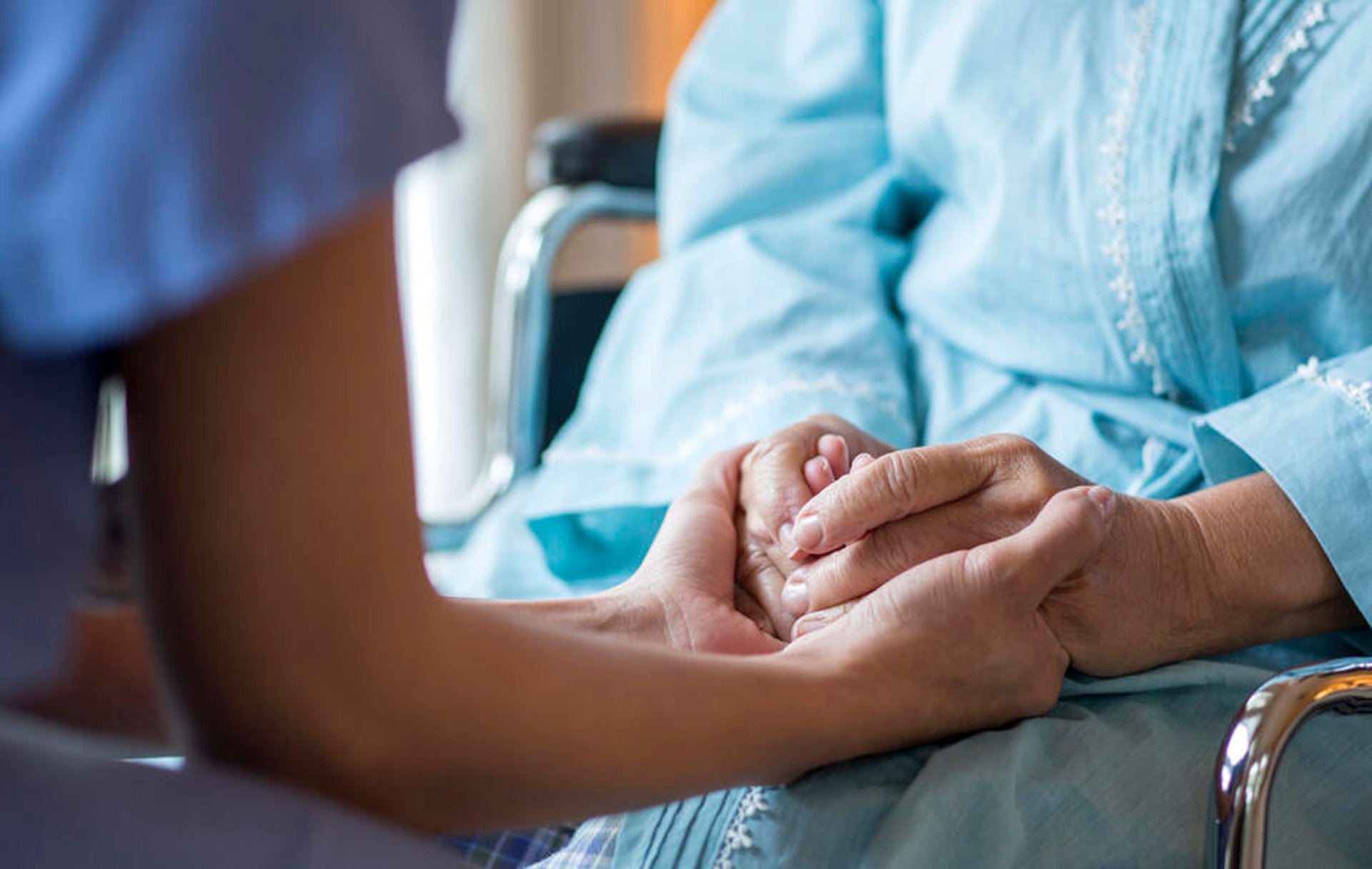 Close up of a nurse comforting an older patient in a wheelchair.