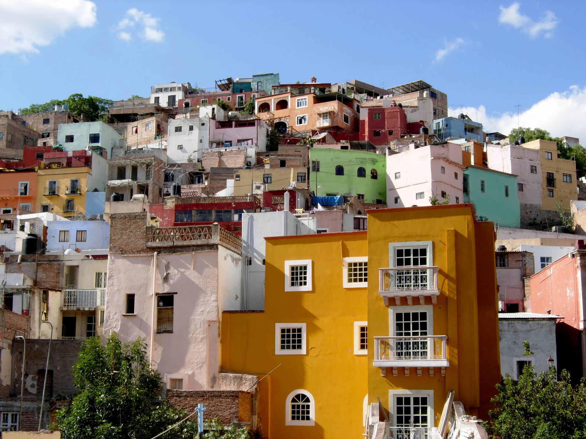A hillside in Mexico with colourful old houses, in yellow, blue, green and white, against a blue sky
