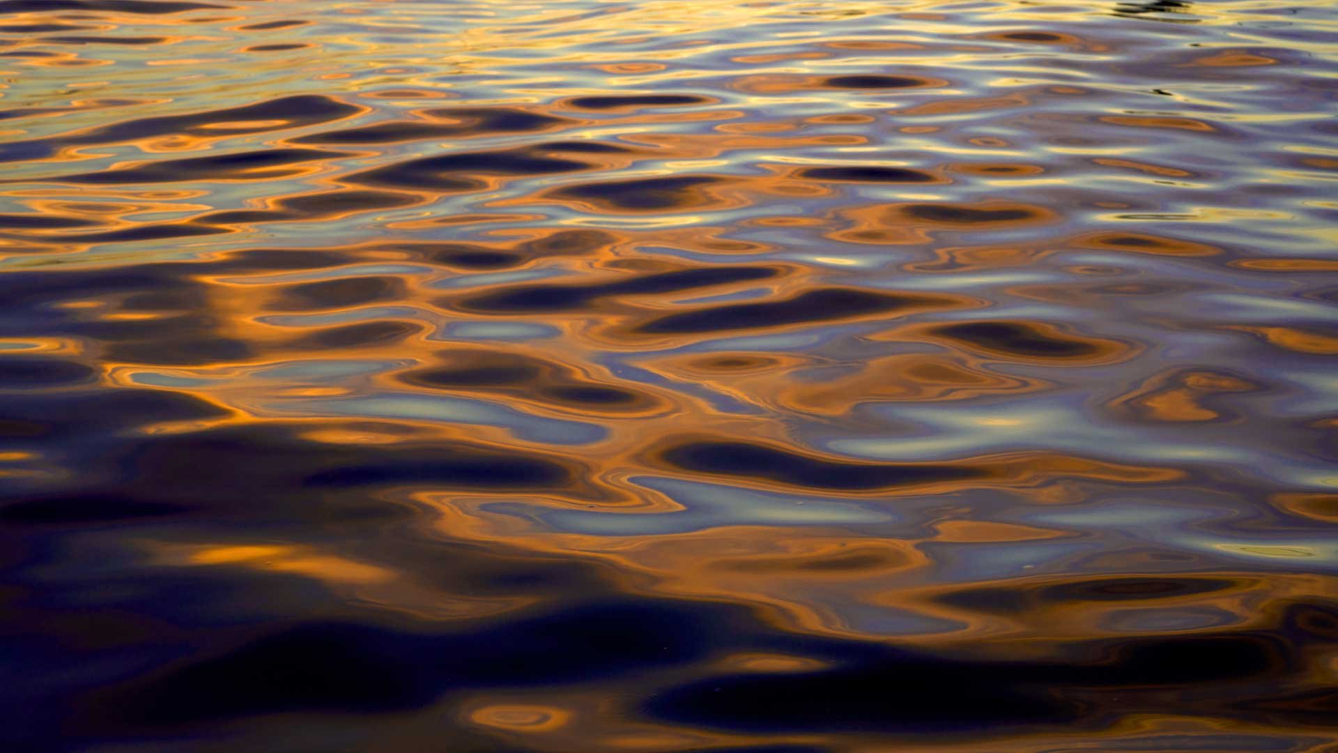 Colours of sunset reflected on a close up view of rippled water.