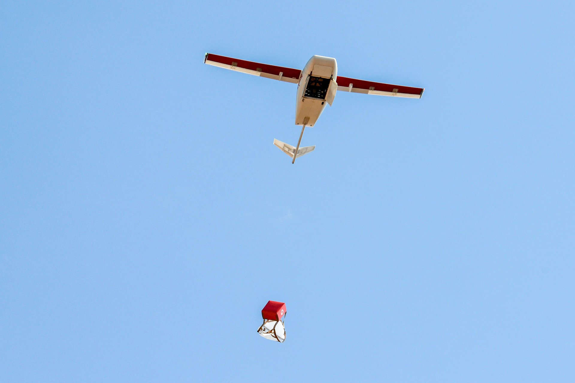 A drone plane dropping a red package with the parachute about to open.