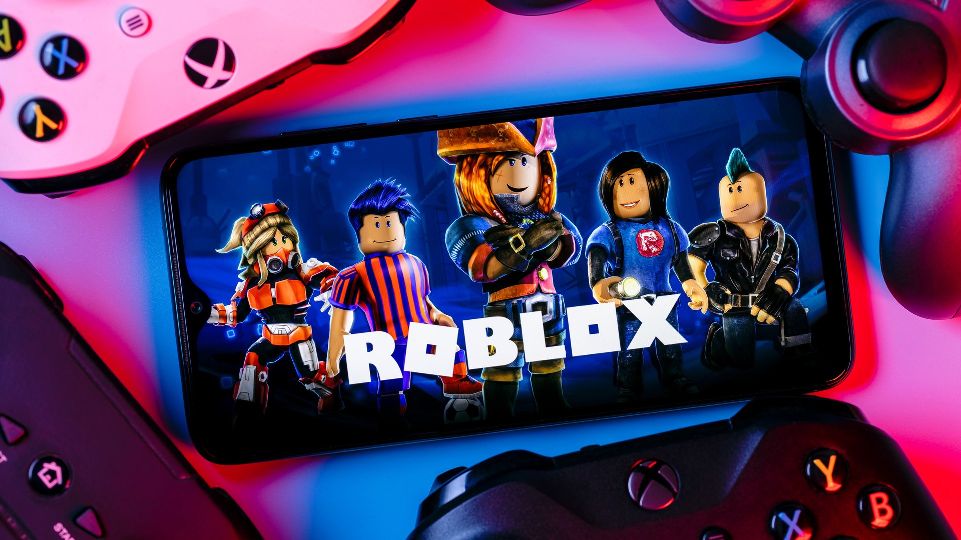 Smartphone displaying Roblox characters, surrounded by colorful gaming controllers.