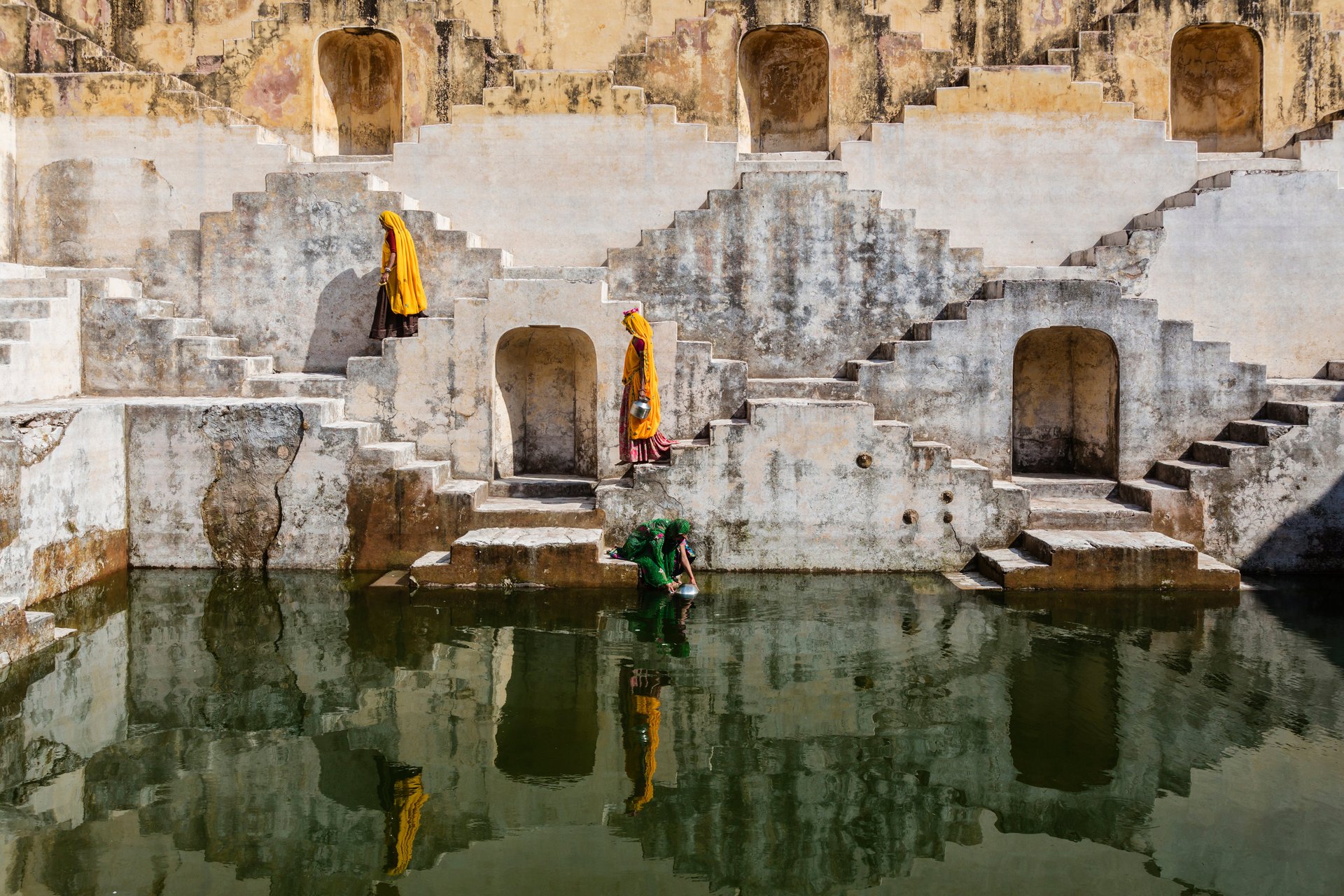 Women in orange saris carrying water at step well in Jaipur, India