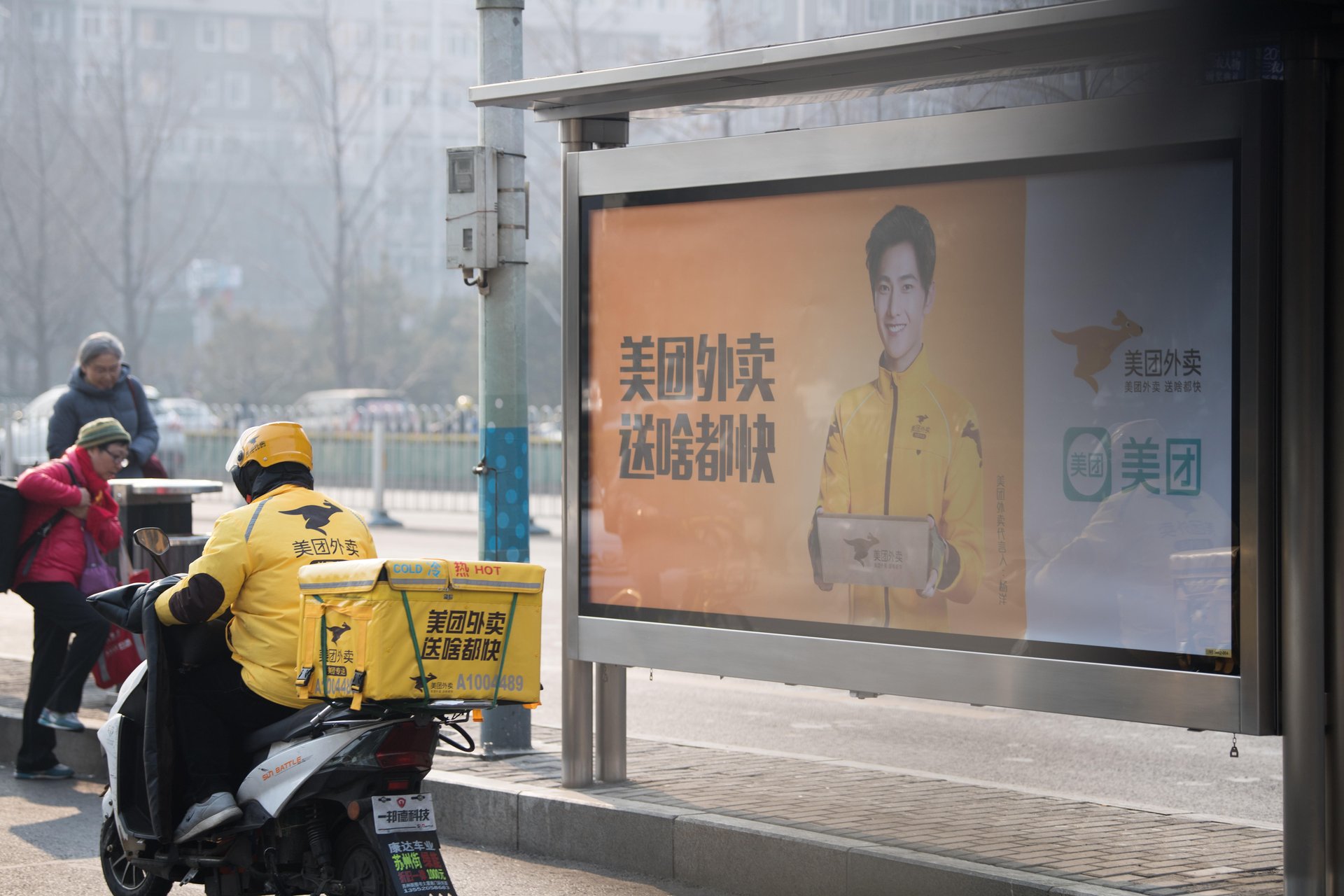 A deliveryman of Chinese online food delivery company Meituan rides past an advertisement for Meituan in Beijing, China.