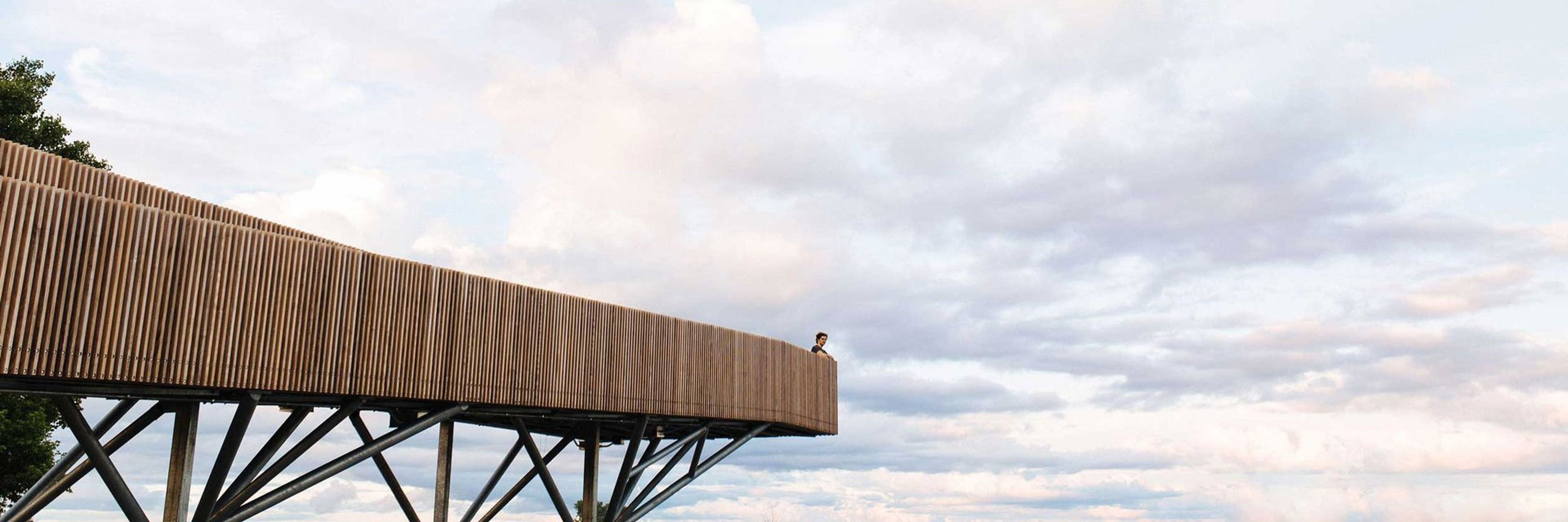 View of person standing on wooden viewpoint on background of amazing sundown cloudy sky.