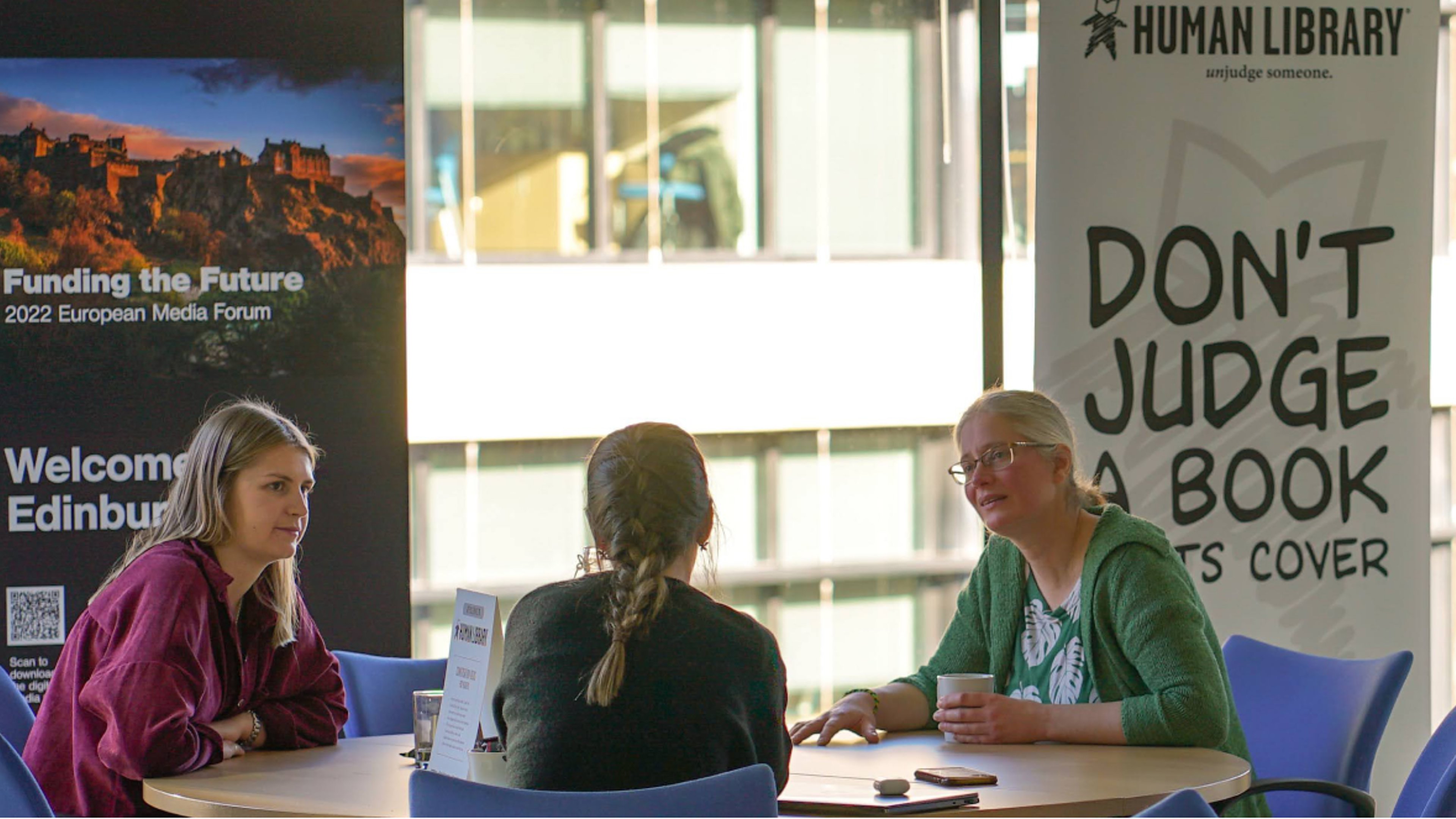 Three people sat round a table with Human Library poster in the background