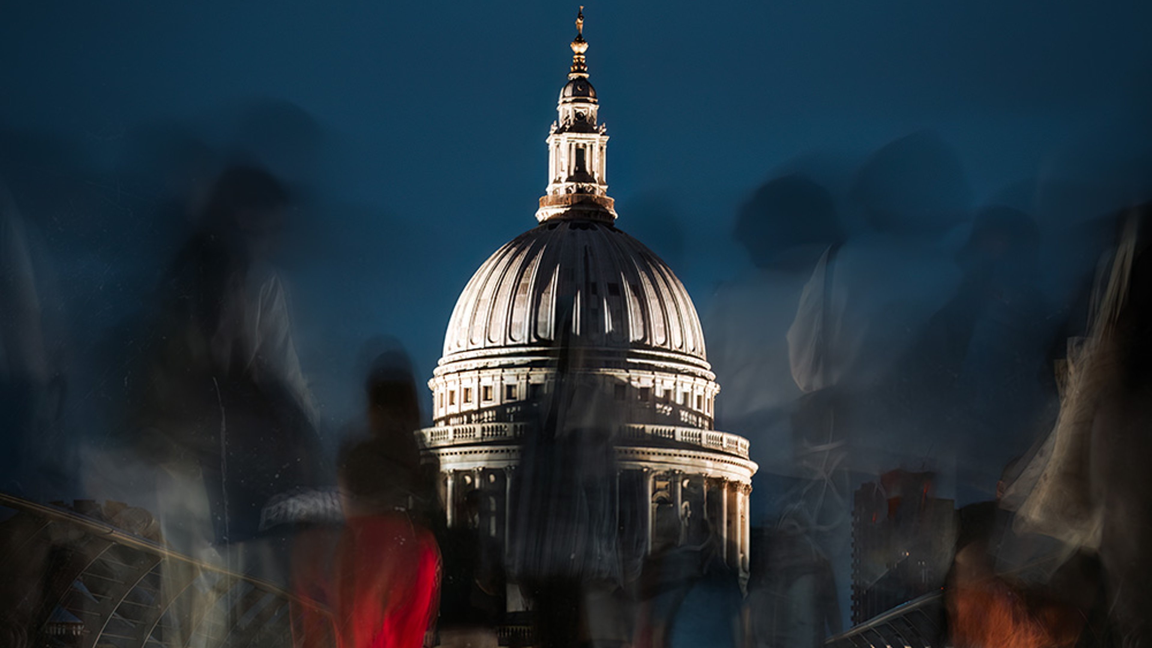 A night time scene of people crossing Millenium Bridge, in front of St Pauls's Cathederal, London.