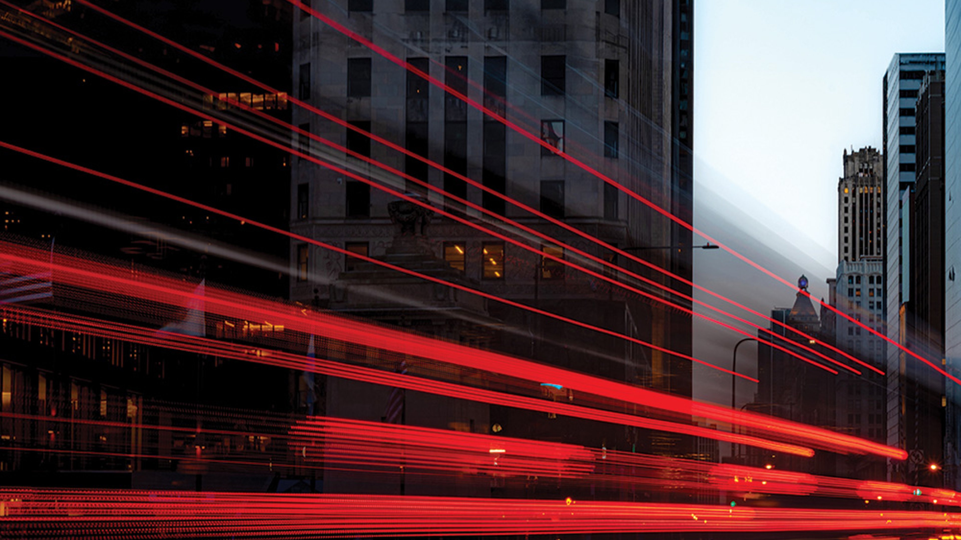 Dusk view of Chicago’s illuminated skyscrapers with red vehicle light trails crossing the city streets.