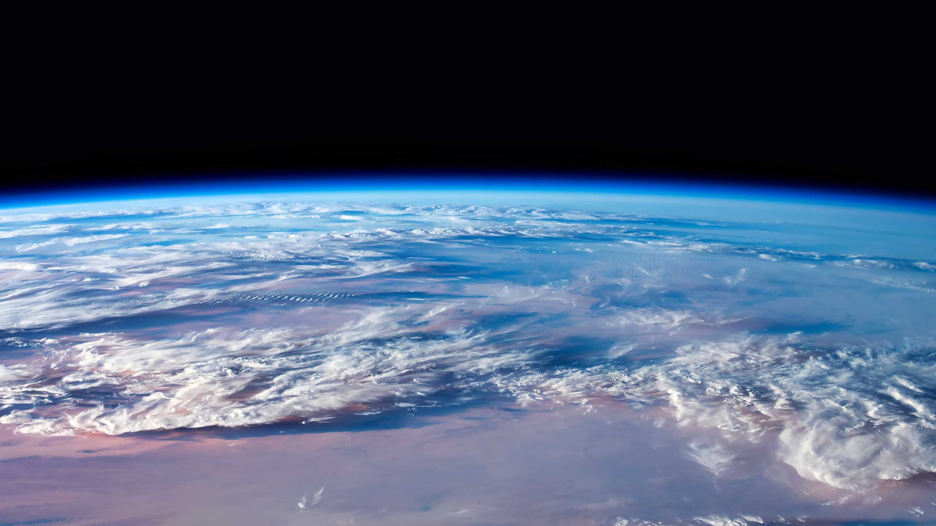 A partial view of the earth from space showing the curvature of the earth and the atmosphere filled with fluffy clouds.