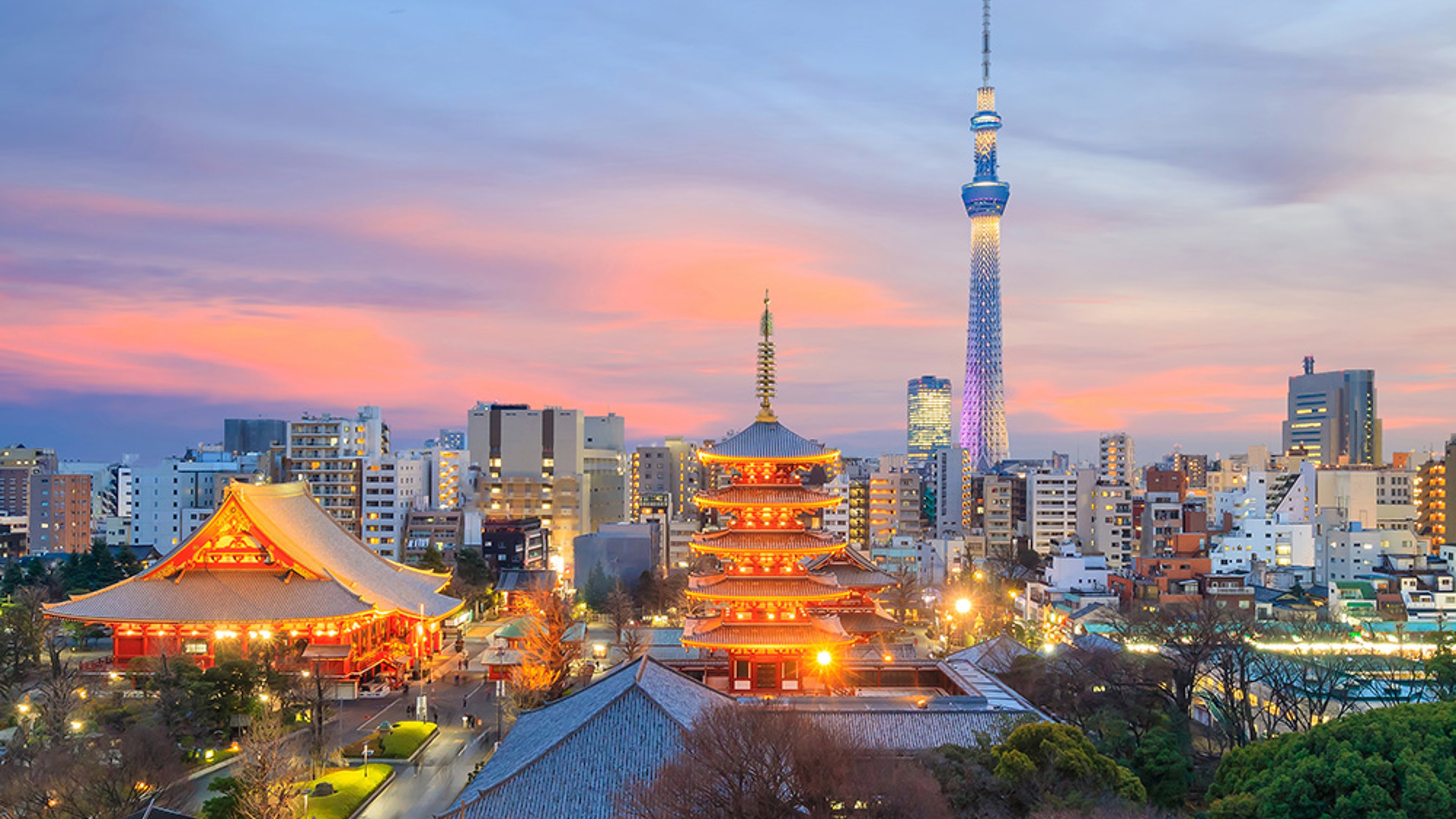 Tokyo skyline at sunset, with a mixture of tradional and contemporary architecture. Hues of blue, pink and orange light the sky.