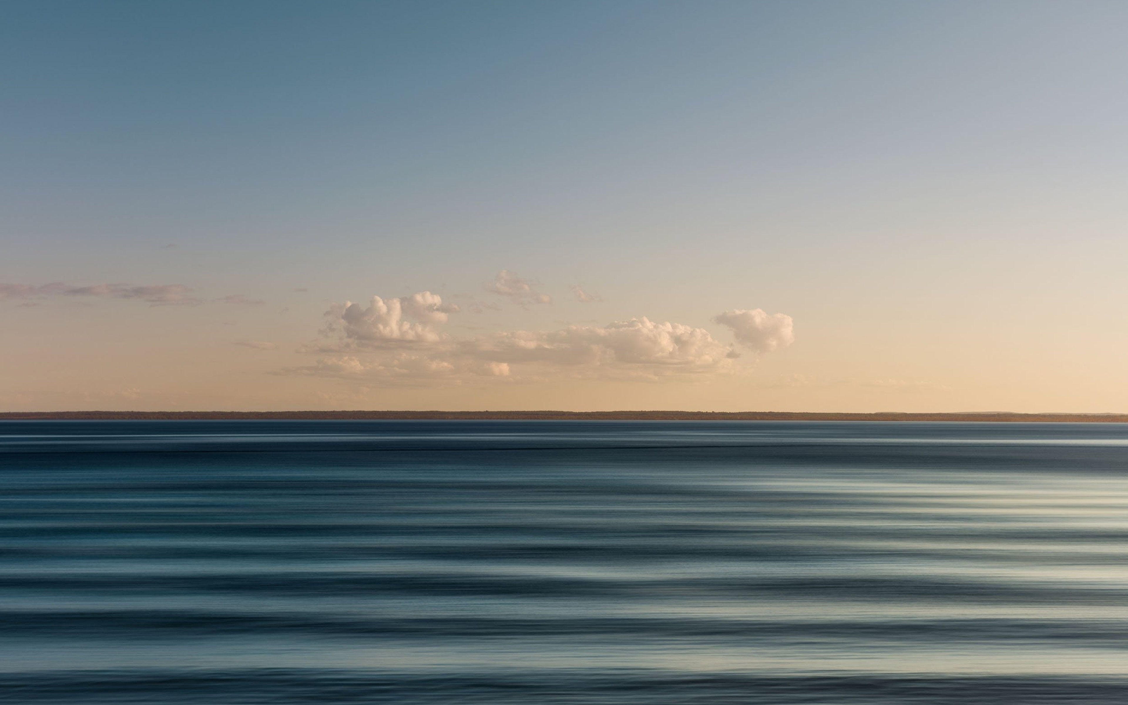 Landscape of a still rippled ocean at dusk in mild weather with clouds across the sky.