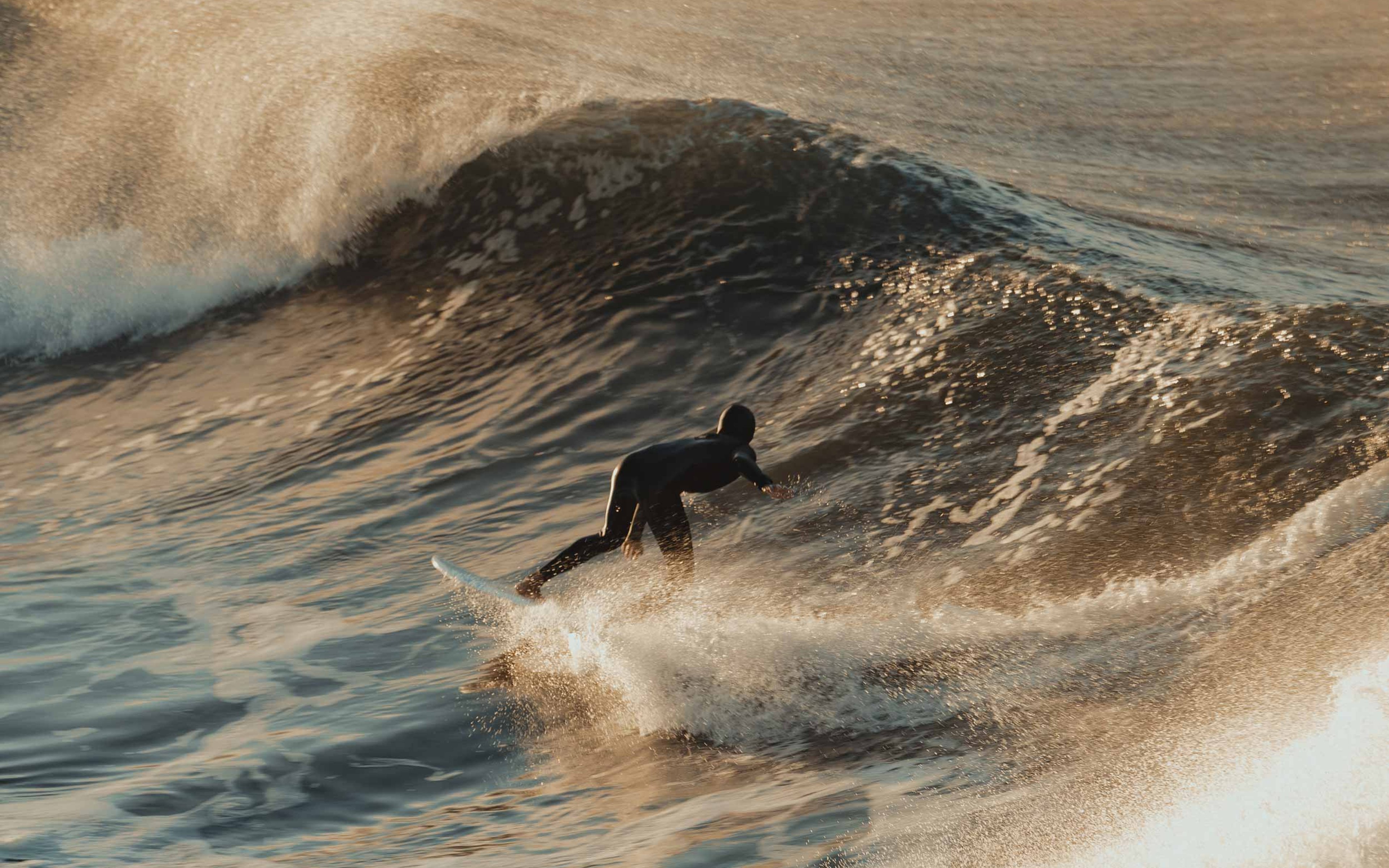 A surfer in the middle of a crashing wave at sunset.