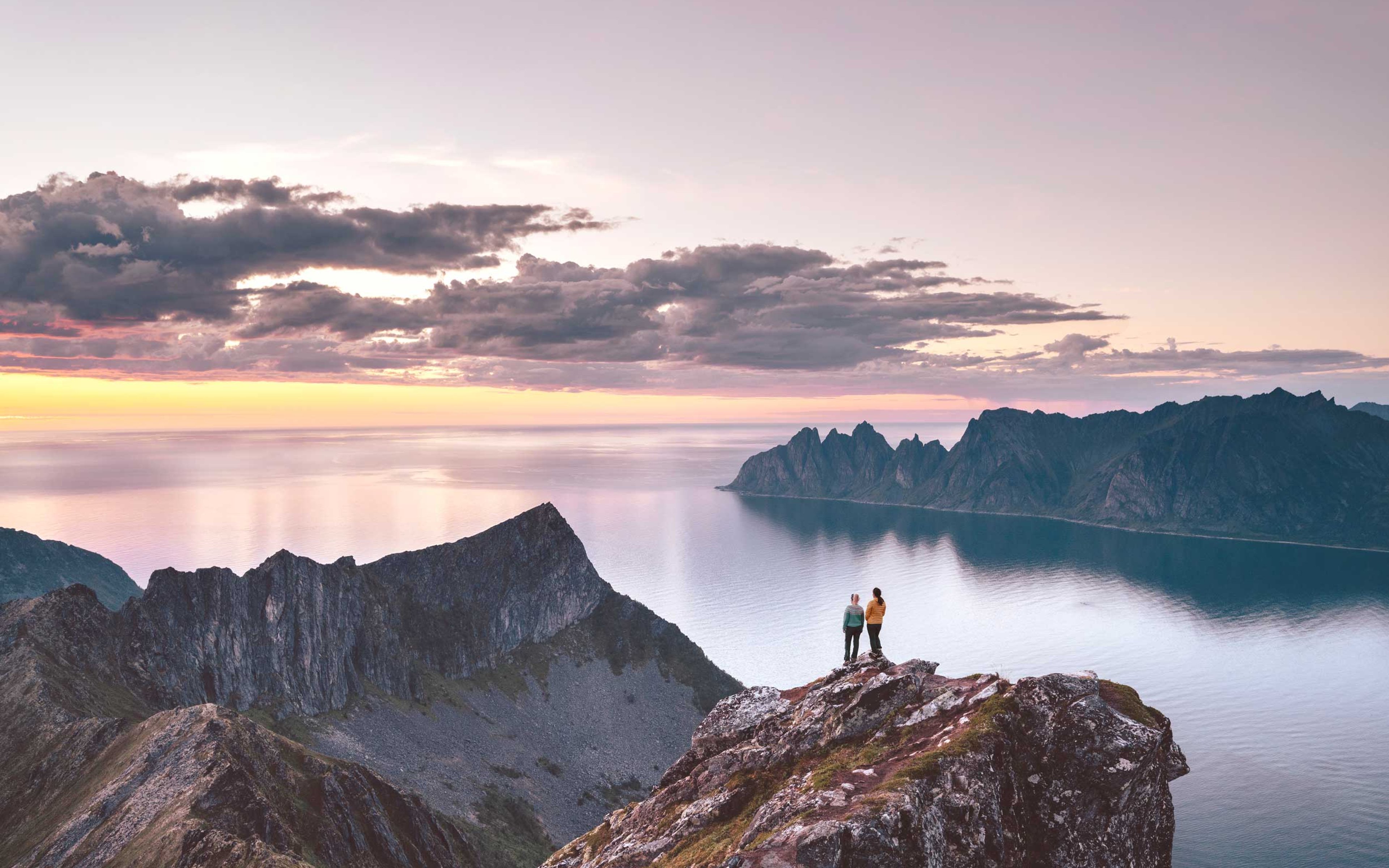 Two people stood on a mountain top admiring the sunset from top of a high cliff in Northern Norway.
