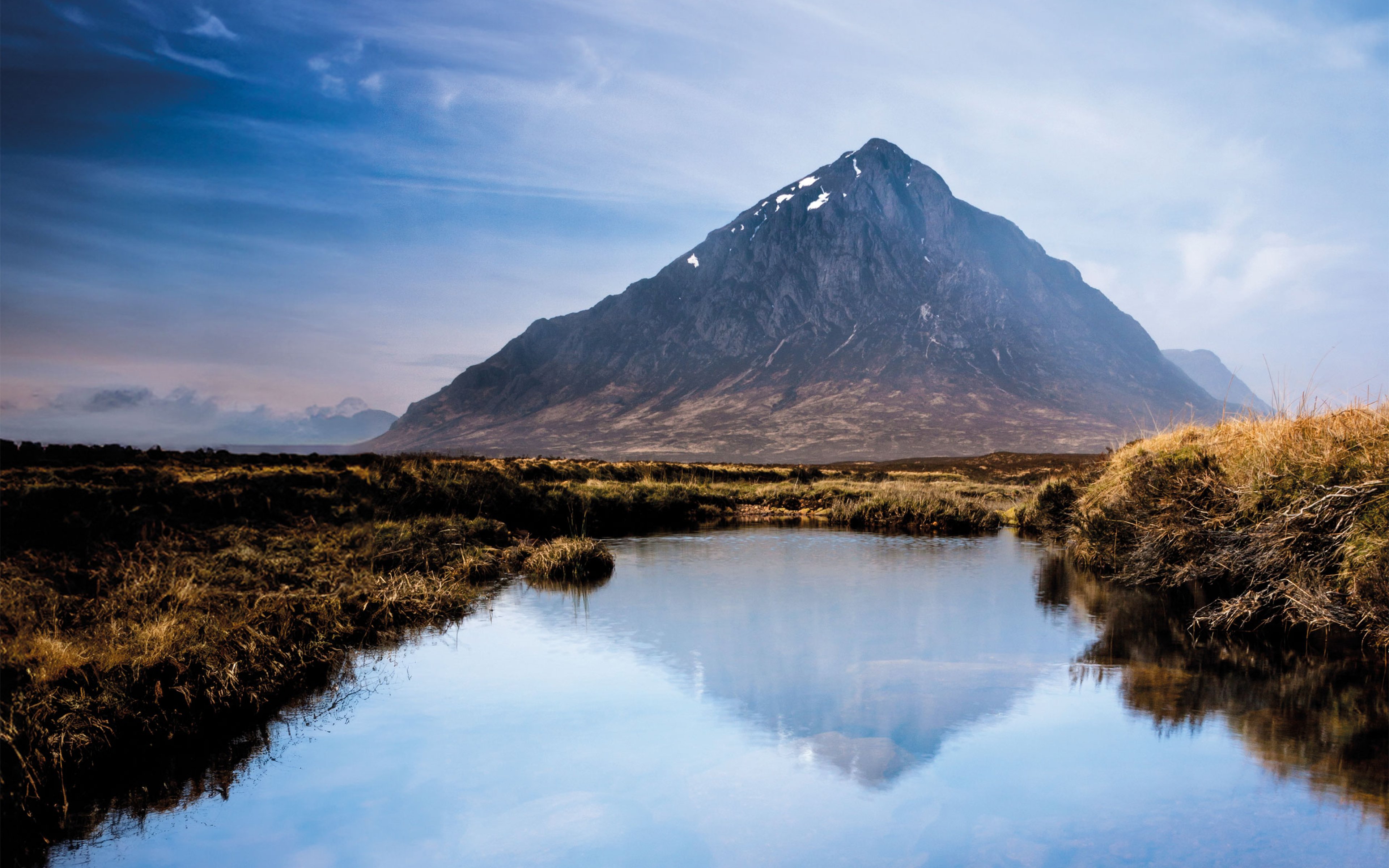 A view of a mountain in the distance reflected in a small loch in the foreground.