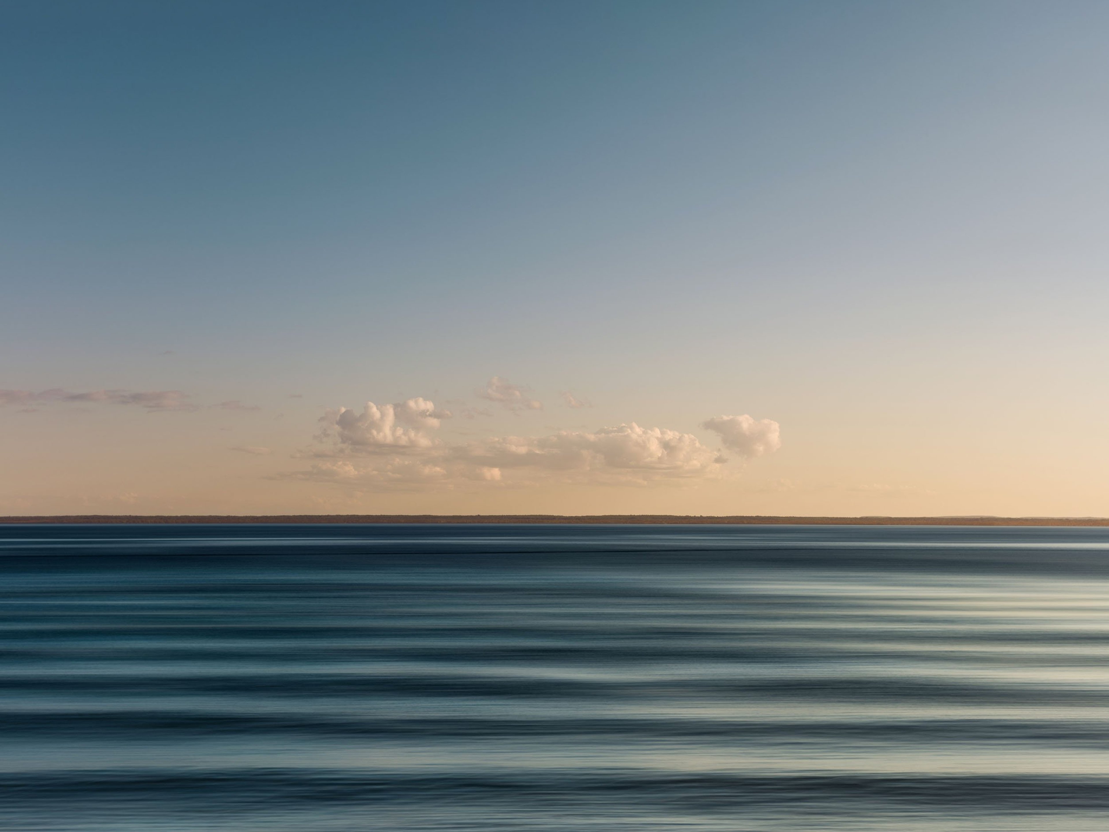 Landscape of a still rippled ocean at dusk in mild weather with clouds across the sky.