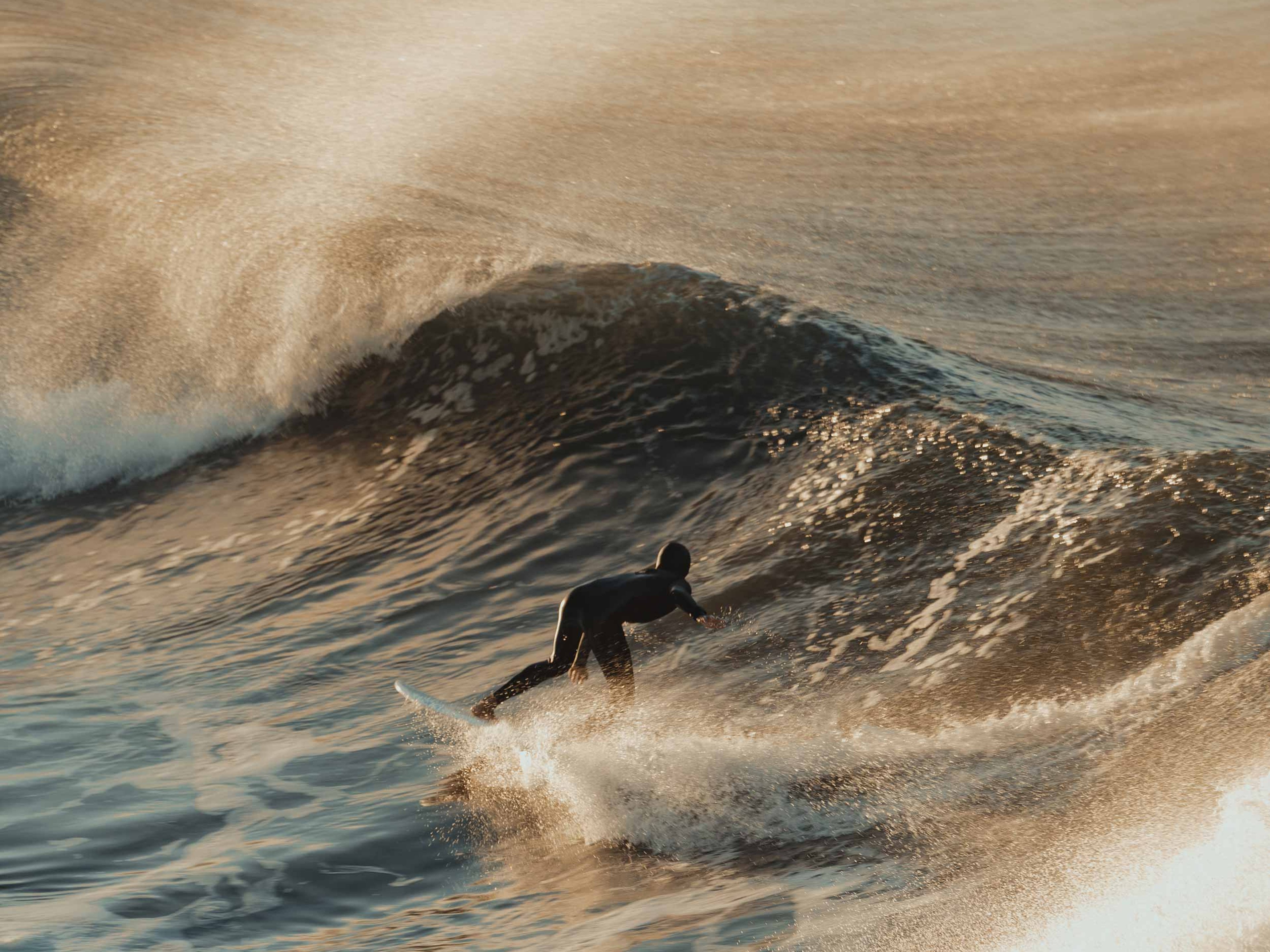 A surfer in the middle of a crashing wave at sunset.