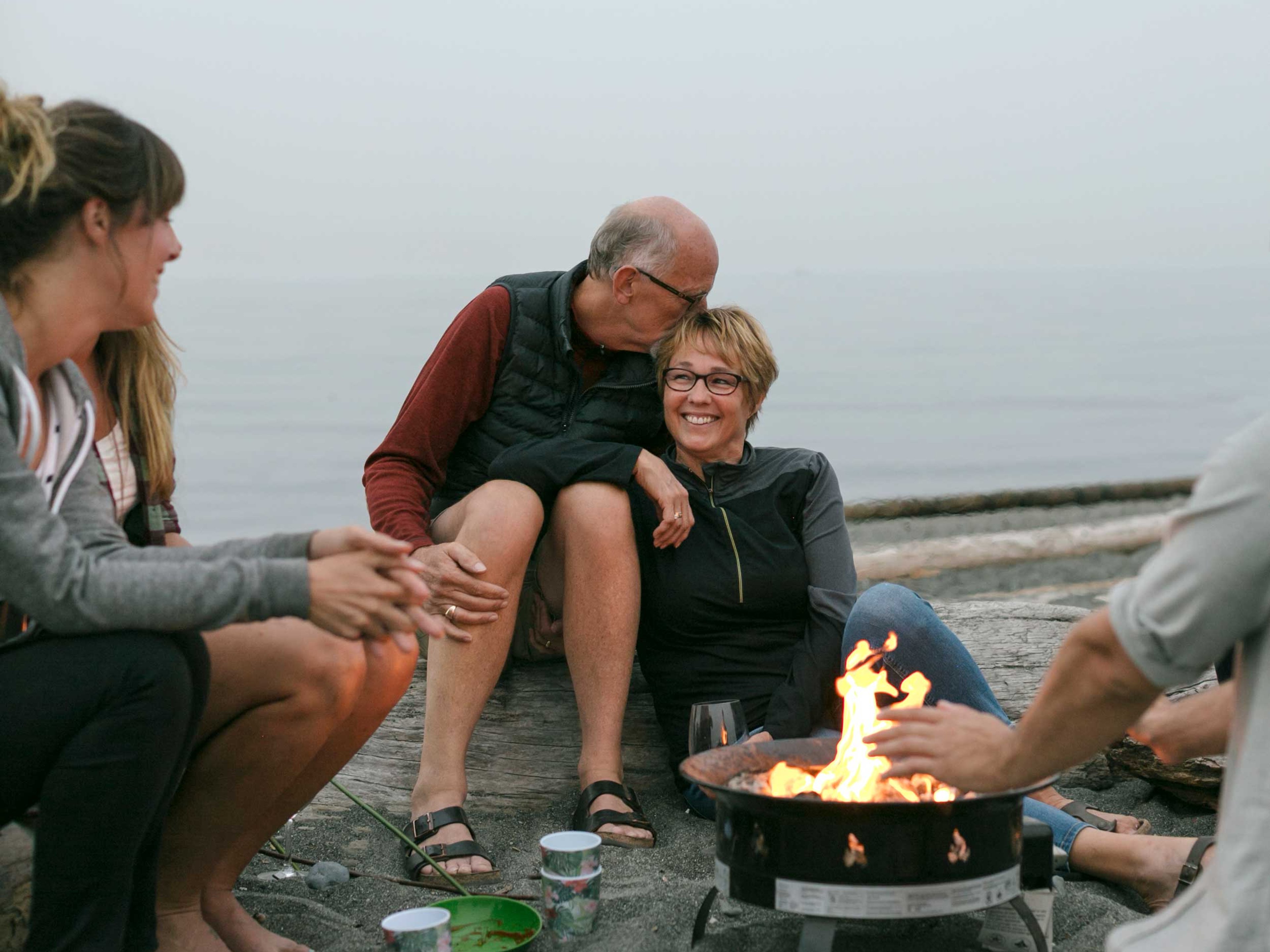 Multi generational family hanging out together around a fire on the beach.