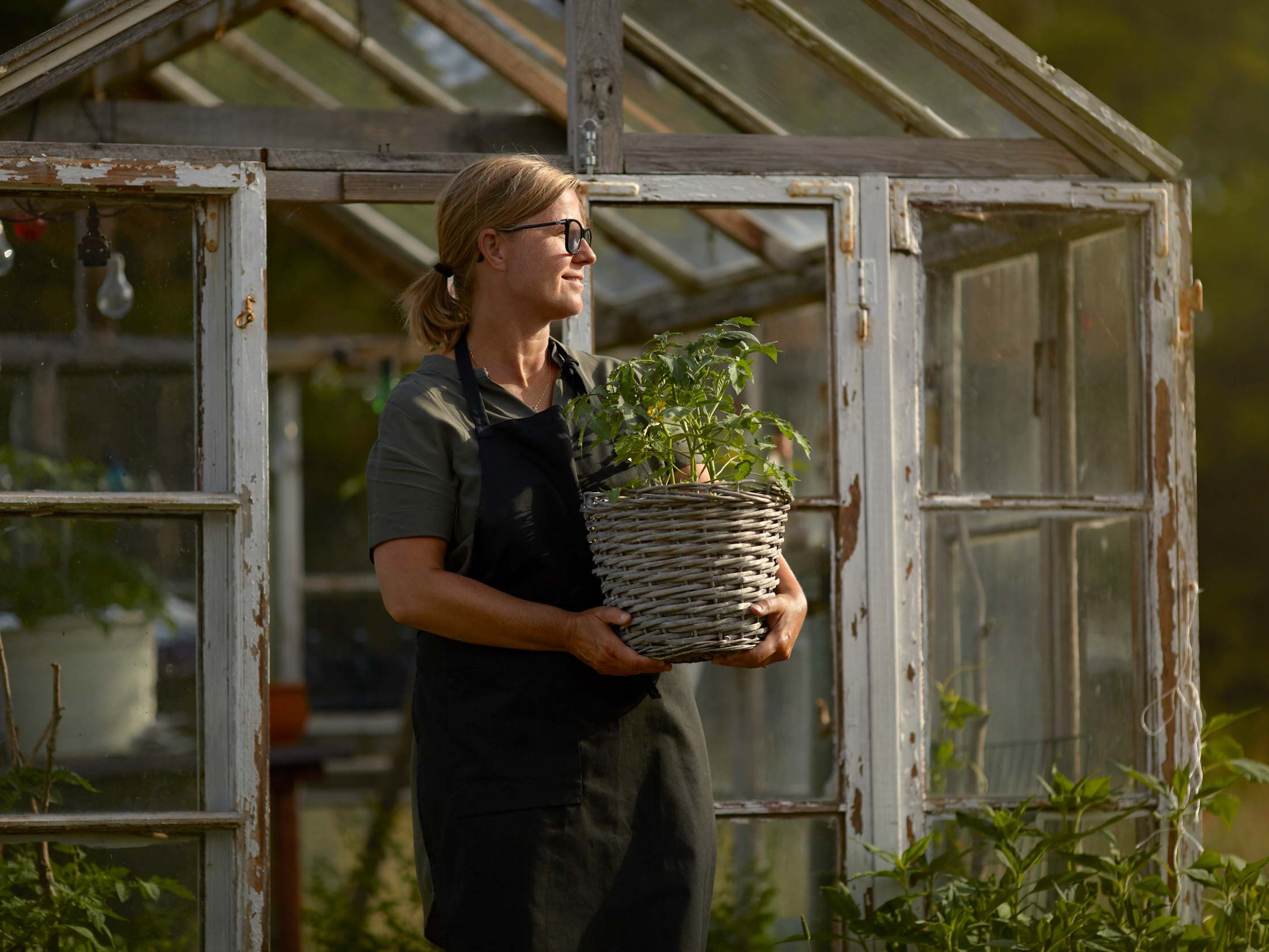A woman holding a plant whilst walking out of a greenhouse.