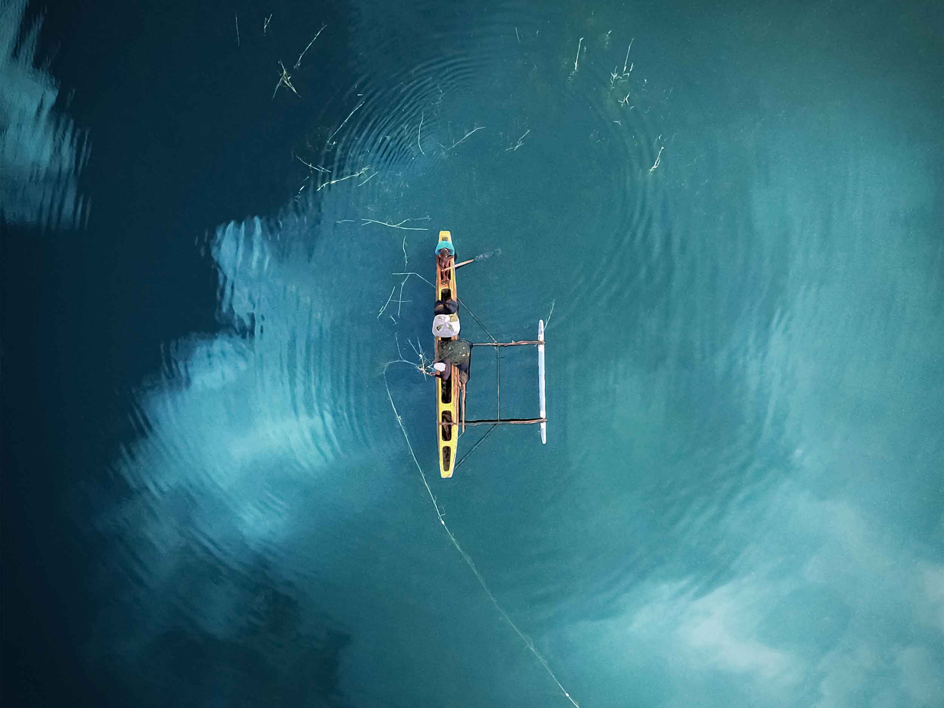 Aerial view of people fishing in traditional outrigger boat in lake with cloud reflections from above in Polonnaruwa, Sri Lanka.