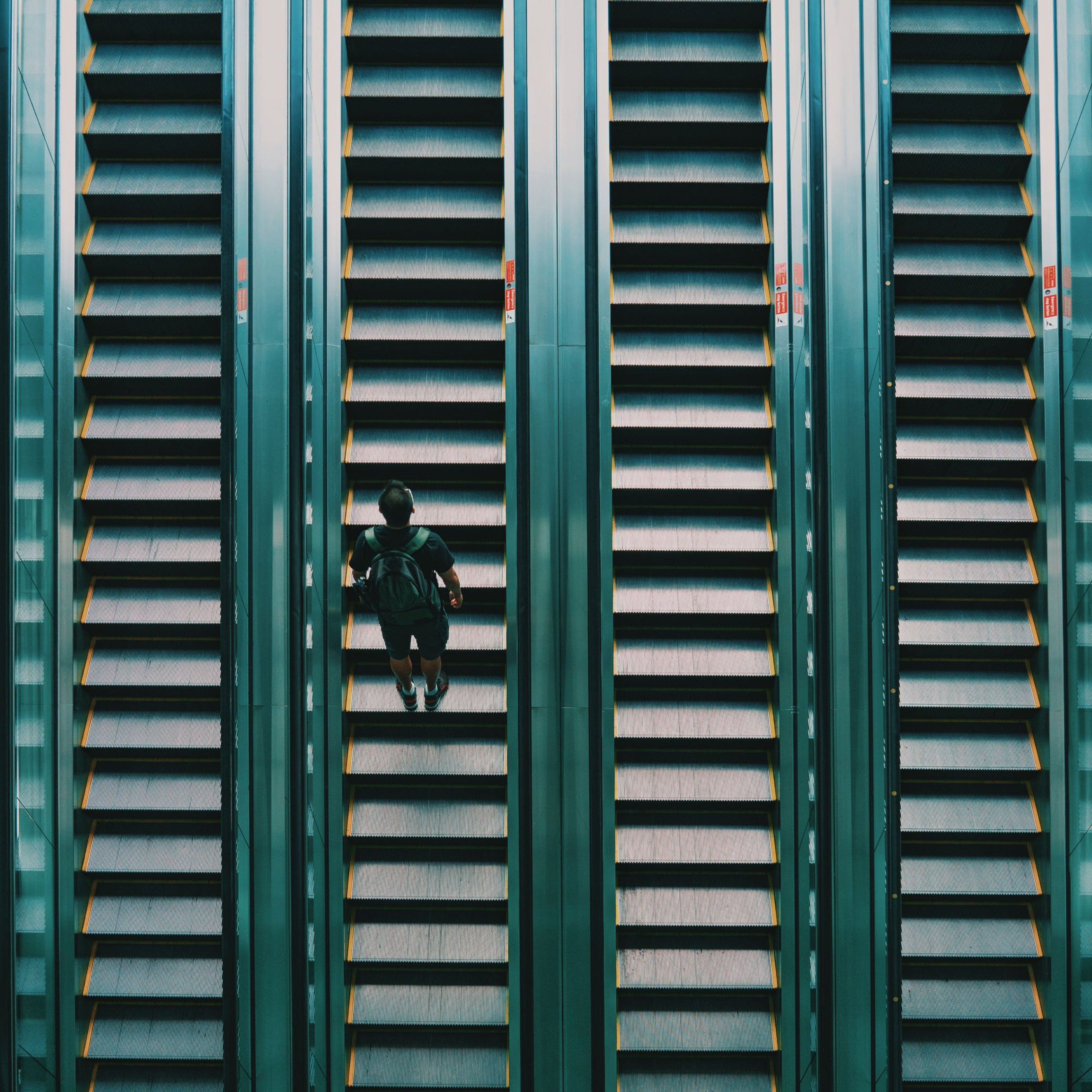 Four escalators with a man wearing a backpack travelling upwards.