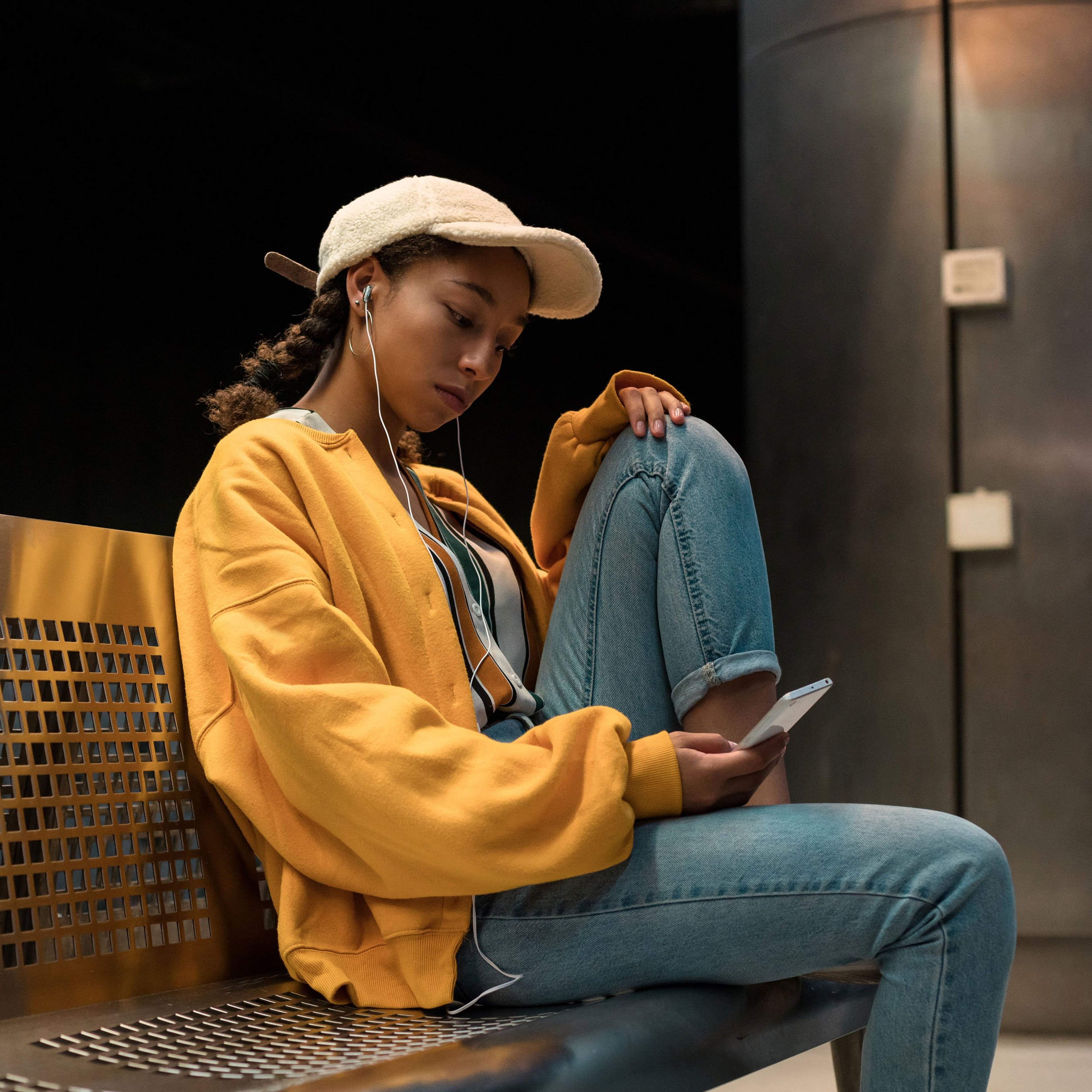 Multiracial teenager listening music with earphones and looking at her phone while waiting for the subway at the station.