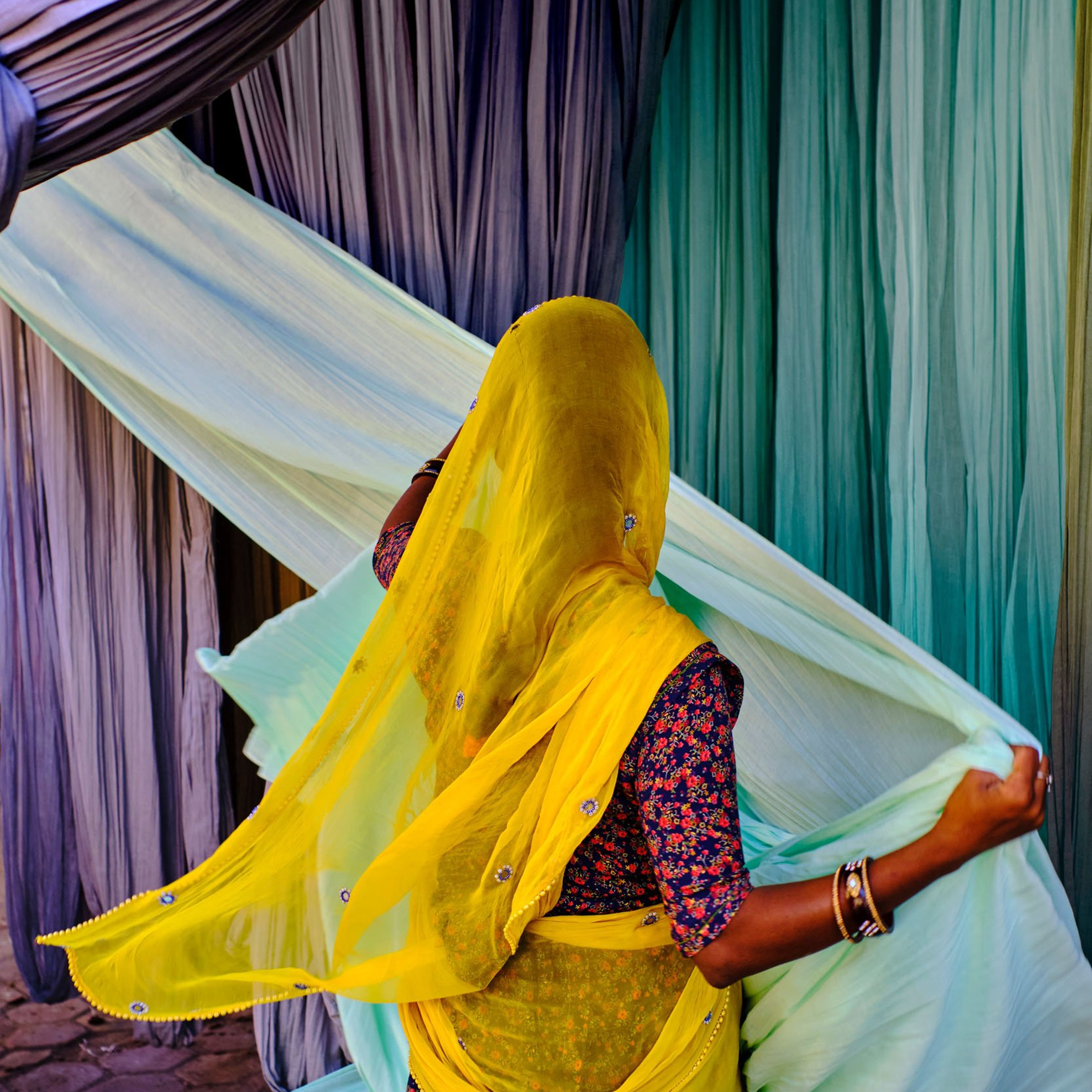 Woman collecting colourful textiles which have been air dried in India.