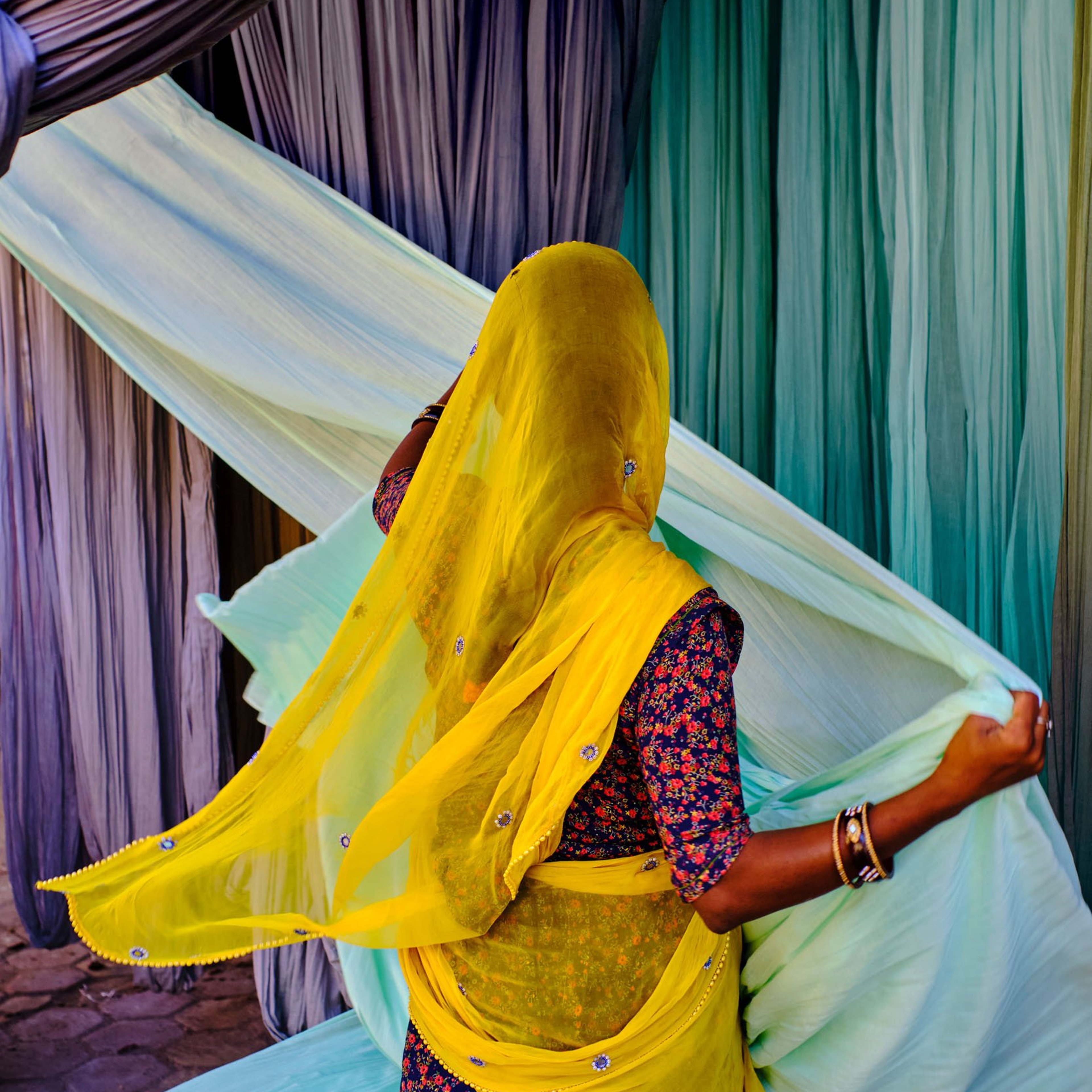 Woman collecting colourful textiles which have been air dried in India.