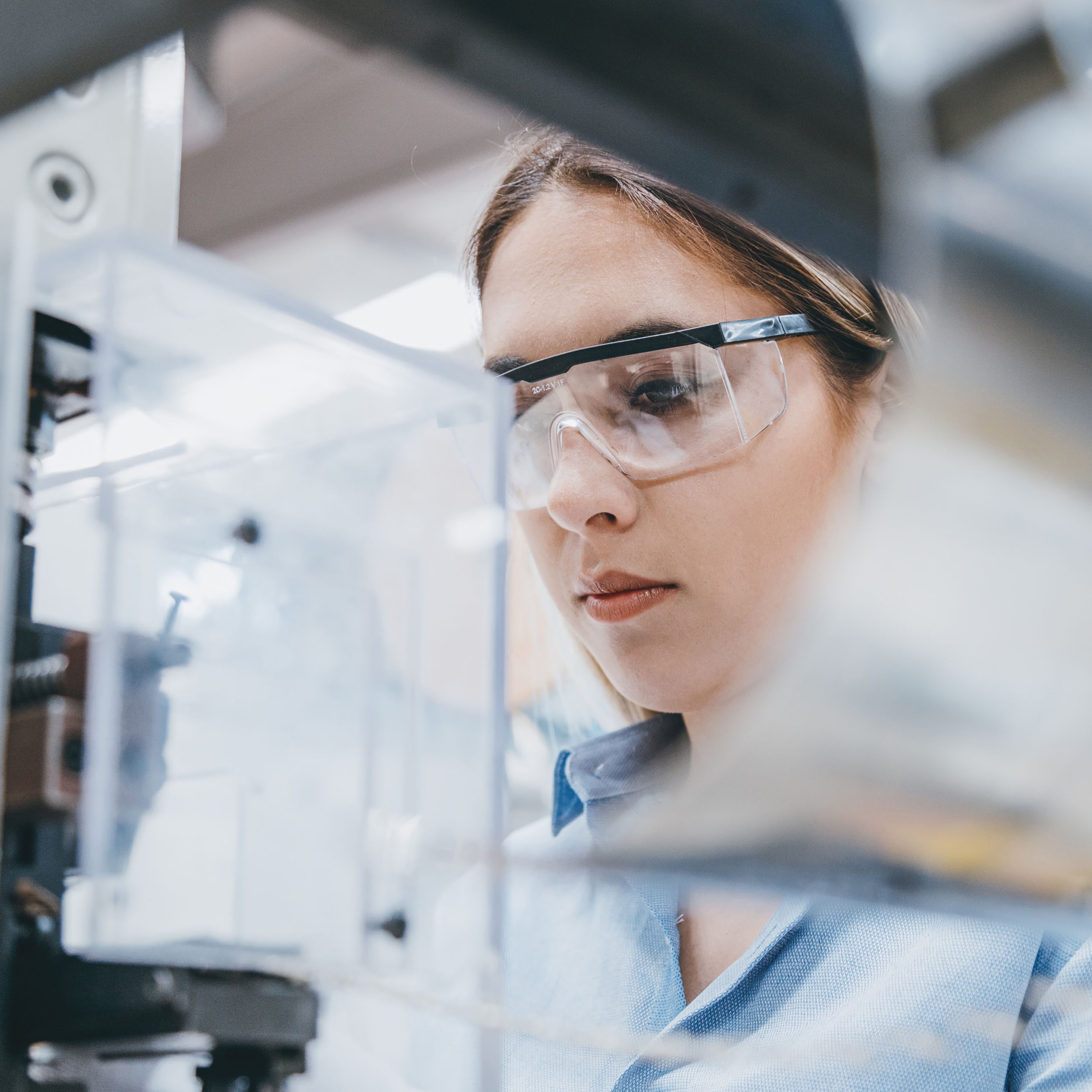 Professional young industrial factory woman inspecting while wearing safety goggles.