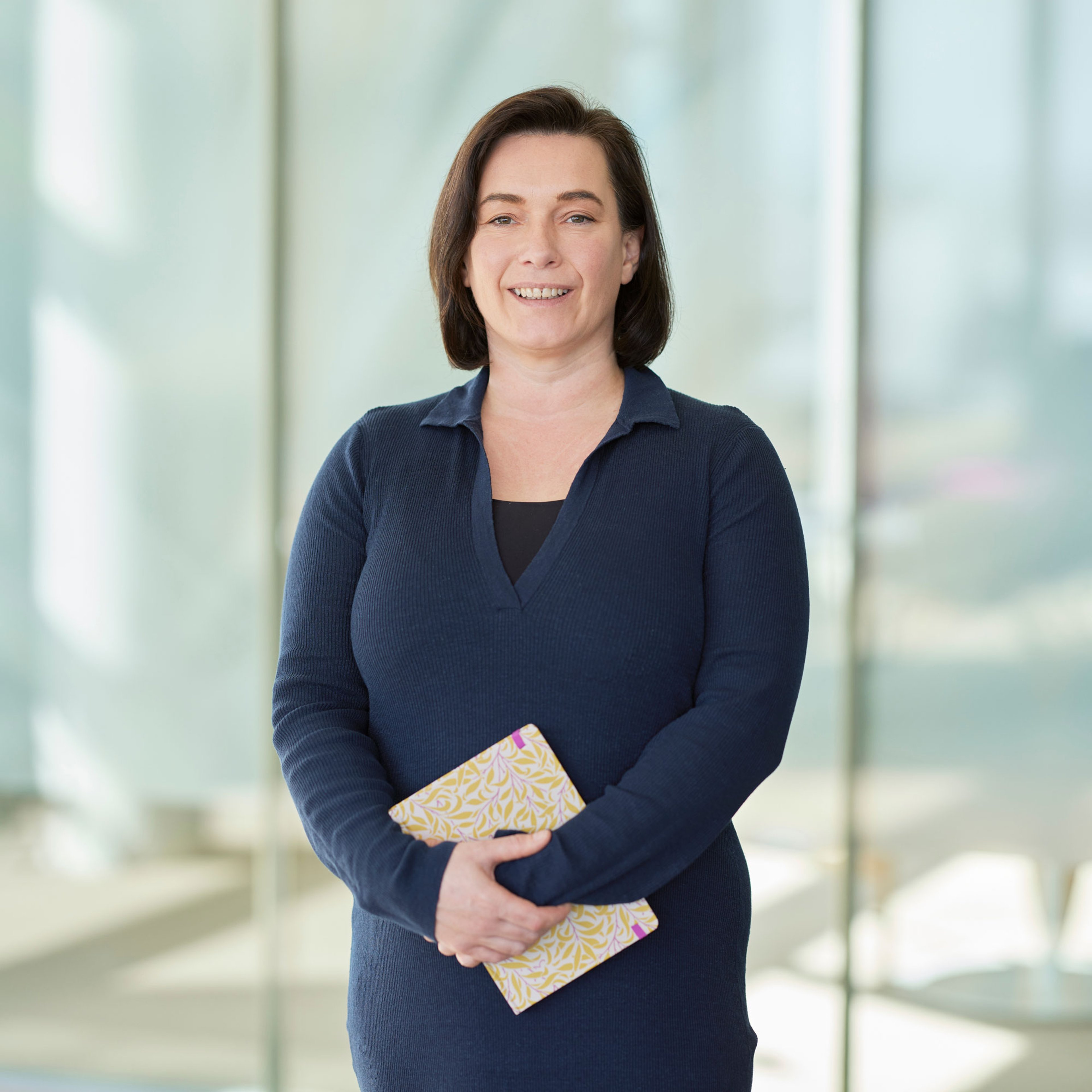 Kathrin Hamilton standing clutching a notepad with both arms in front.