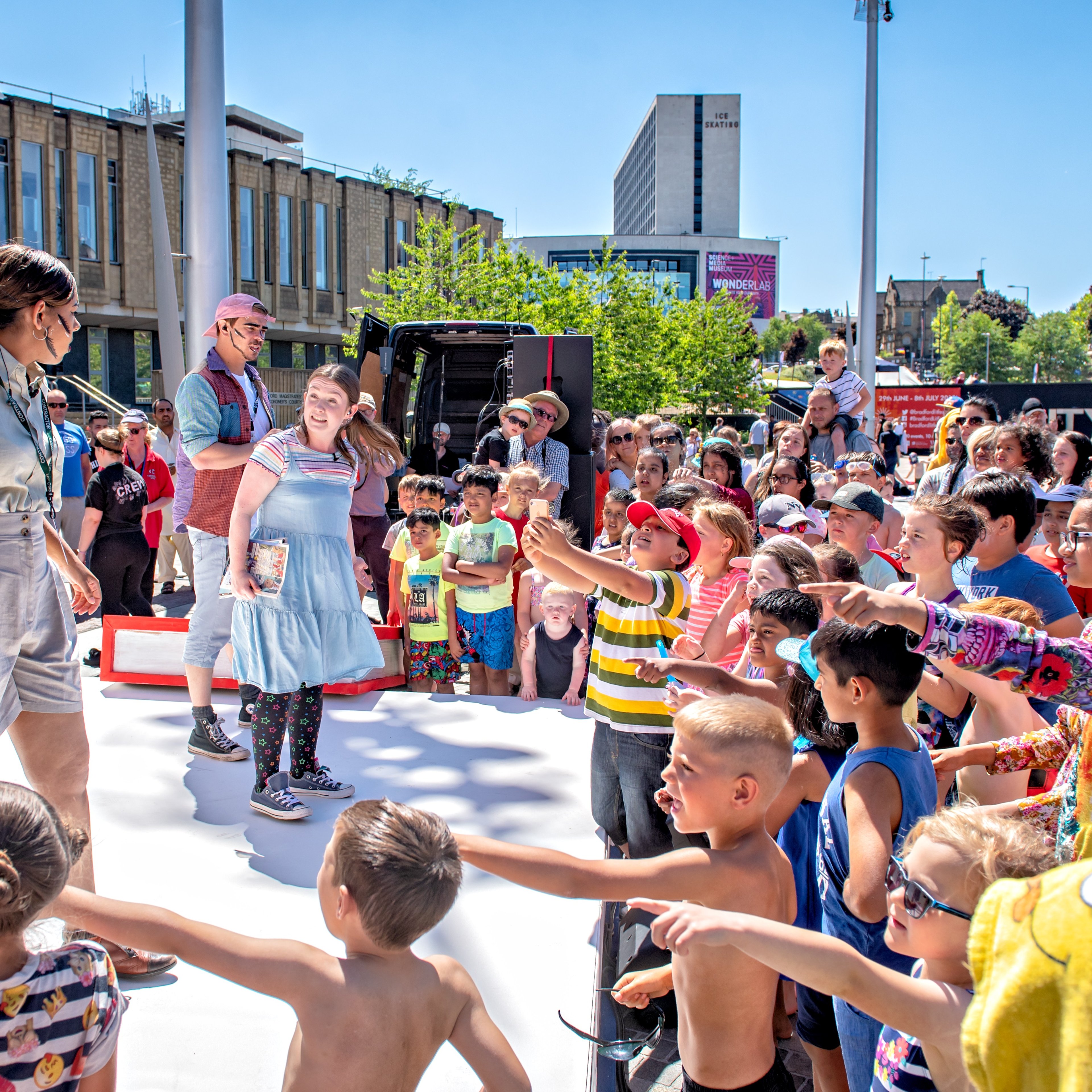 An outside stage with performers in front of a crowd of children.
