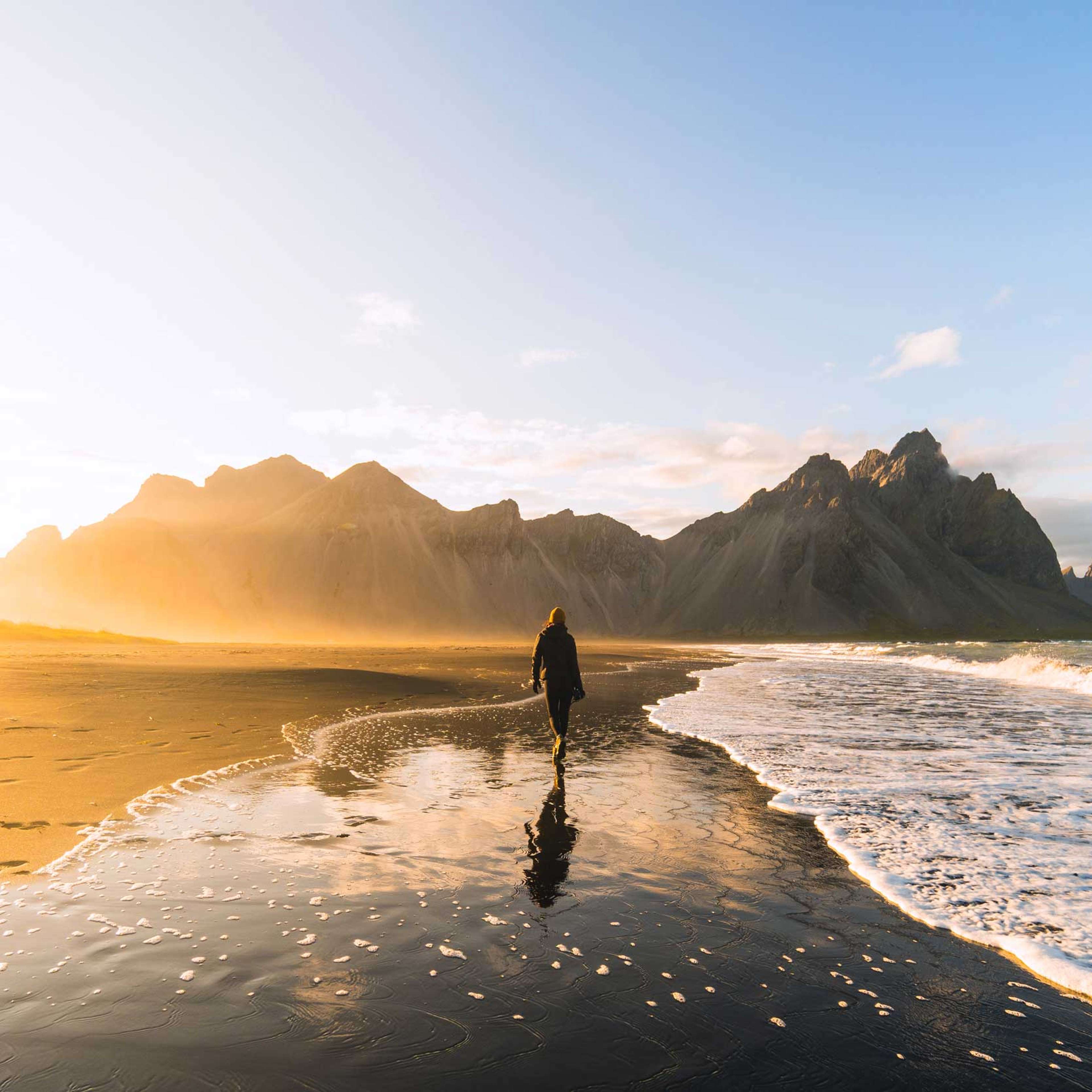 Woman walking on a beach with black sand in Iceland at sunset.